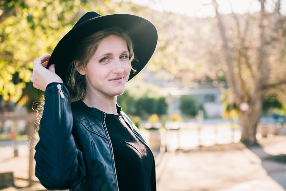A woman in a black hat and leather jacket smiles in the warm autumn sunlight.
