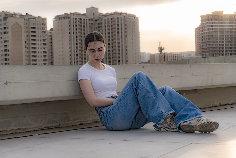 Woman sitting on a rooftop in cityscape during sunset, exuding a calm and contemplative mood.