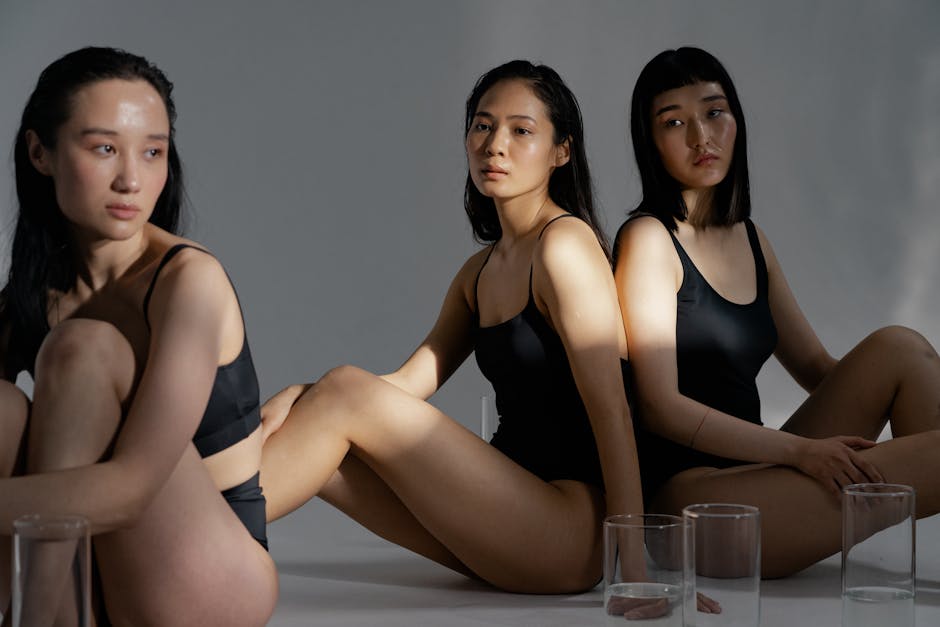 Three Asian women in black swimwear pose artistically with soft lighting.