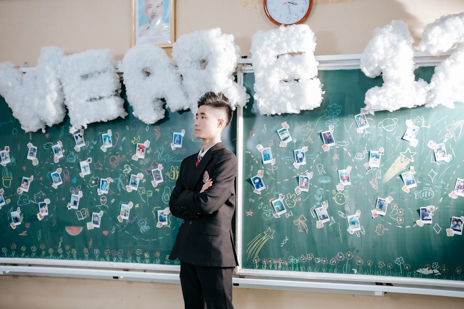 Young man in formal attire celebrates graduation in a creatively decorated classroom.